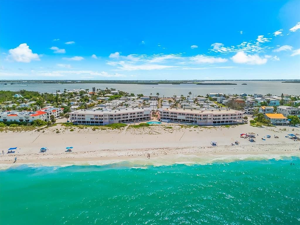 Aerial view of the Anna Maria Island Club at 2600 Gulf Dr N, a low-rise beachfront condo building set on the white sand of Bradenton Beach with turquoise Gulf water in the foreground and the intracoastal bay behind